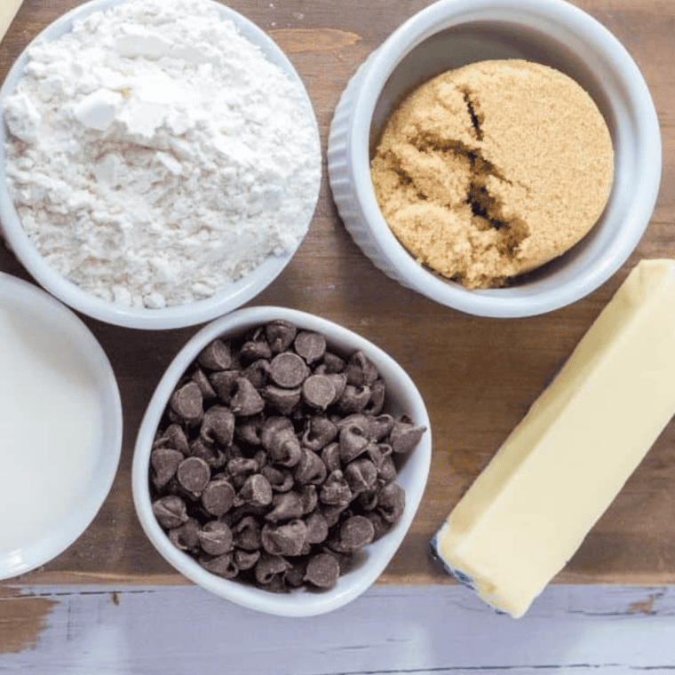 Ingredients for air fryer chocolate chip muffins measured into bowls on a table — flour, sugar, egg, milk, butter, vanilla, and chocolate chips