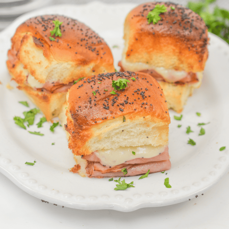 Plate of golden-brown air fryer King's Hawaiian ham and cheese sliders topped with poppy seeds
