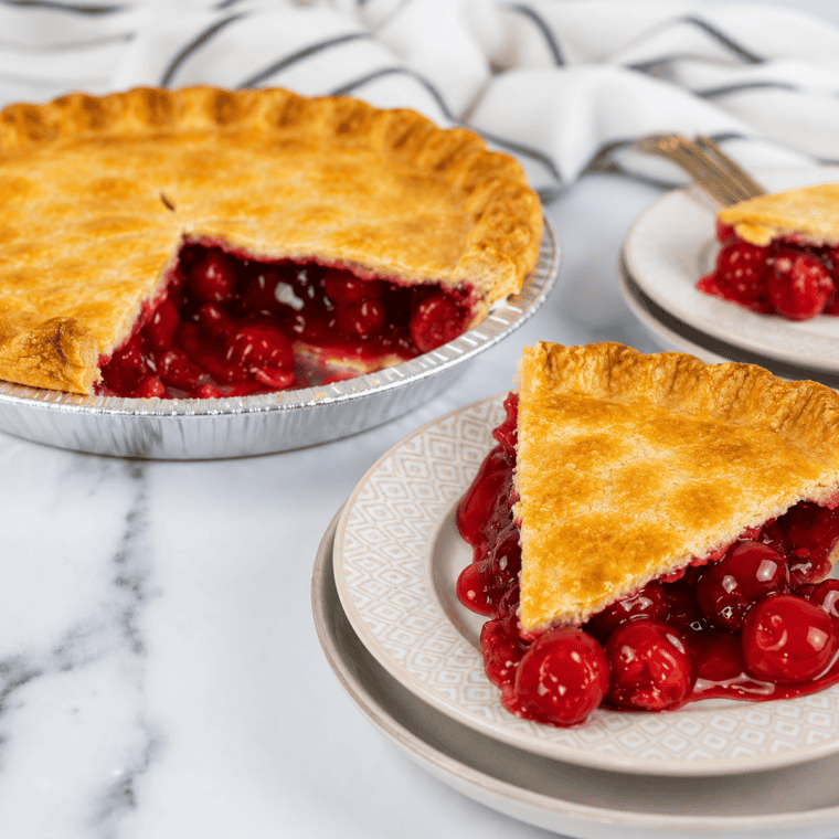 Whole air fryer cherry pie on a plate with one slice removed, showing the cherry filling