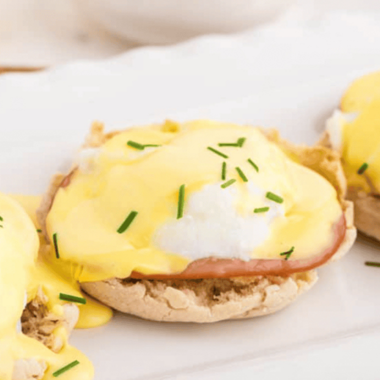 Air fryer eggs benedict with poached eggs, ham, and hollandaise on toasted English muffins.