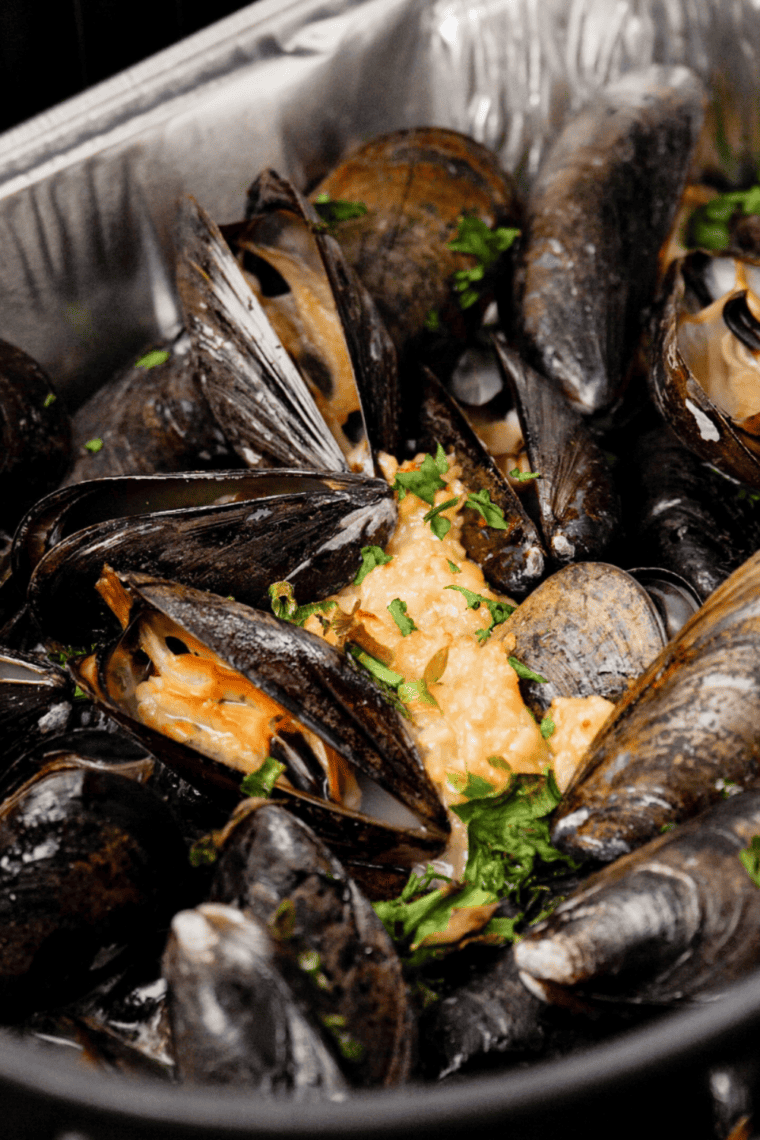 Seasoned mussels arranged in a single layer inside air fryer basket for even cooking.