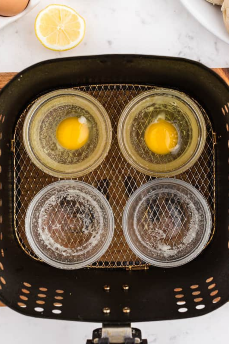 Air fryer poaching eggs in greased ramekins with water cooking at 360°F until set whites and runny or firm yolks then gently releasing onto English muffins for Eggs Benedict