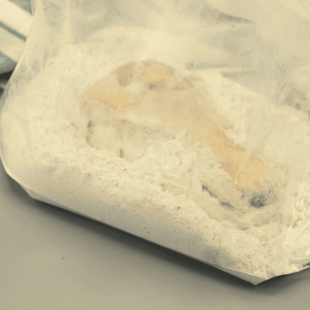 Chicken being dredged in Kentucky Kernel seasoned flour in a zip-top bag for air fryer fried chicken