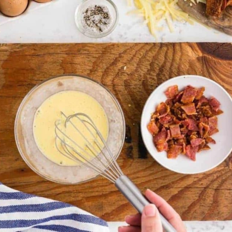 whisking bowl of egg and cream next to bowl of bacon crumbles