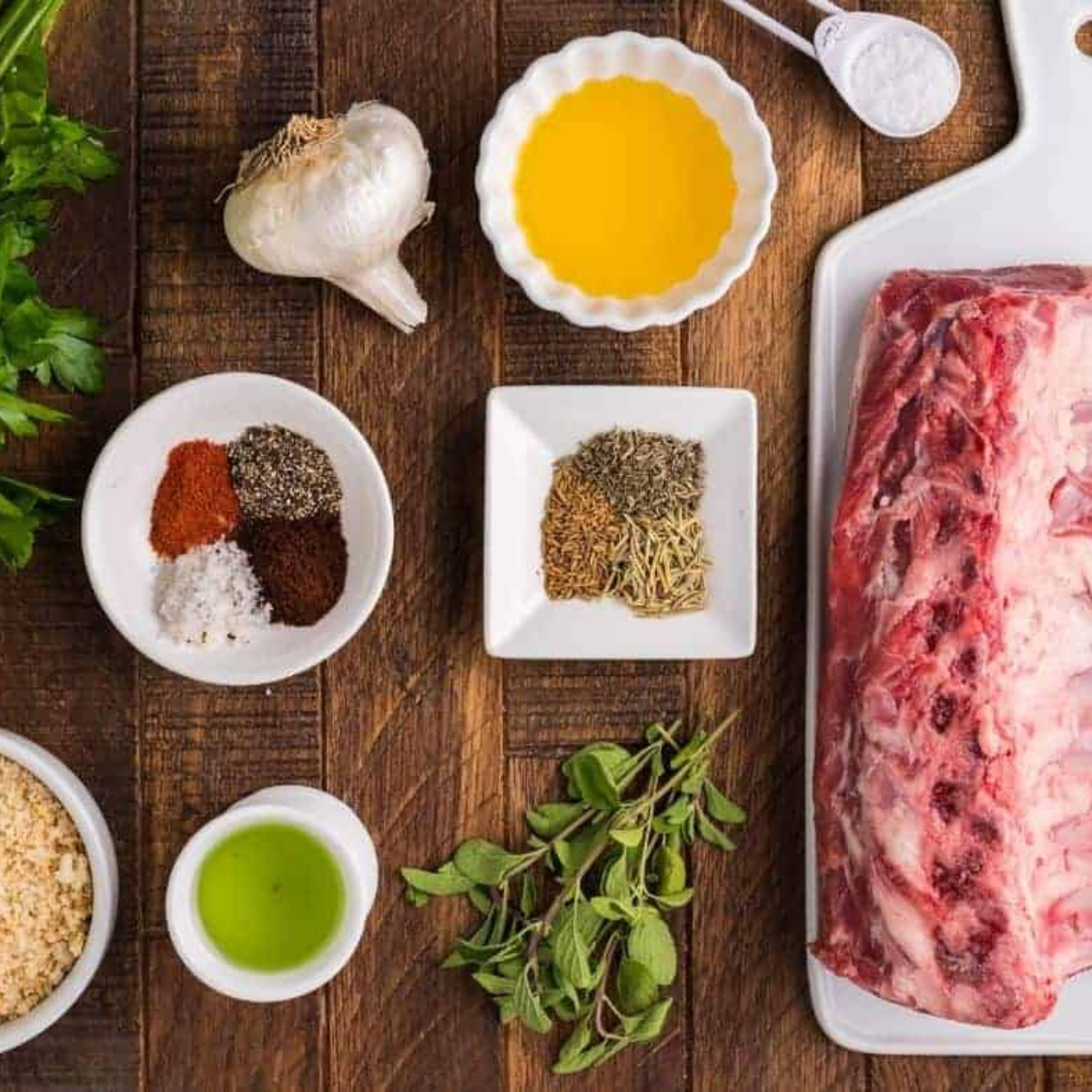 Ingredients for air fryer rack of lamb, including a raw lamb rack, olive oil, garlic, rosemary, thyme, salt, and pepper