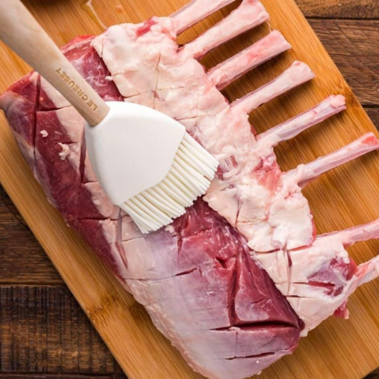 Rack of lamb trimmed and patted dry next to a bowl of garlic, salt, pepper, rosemary, and thyme