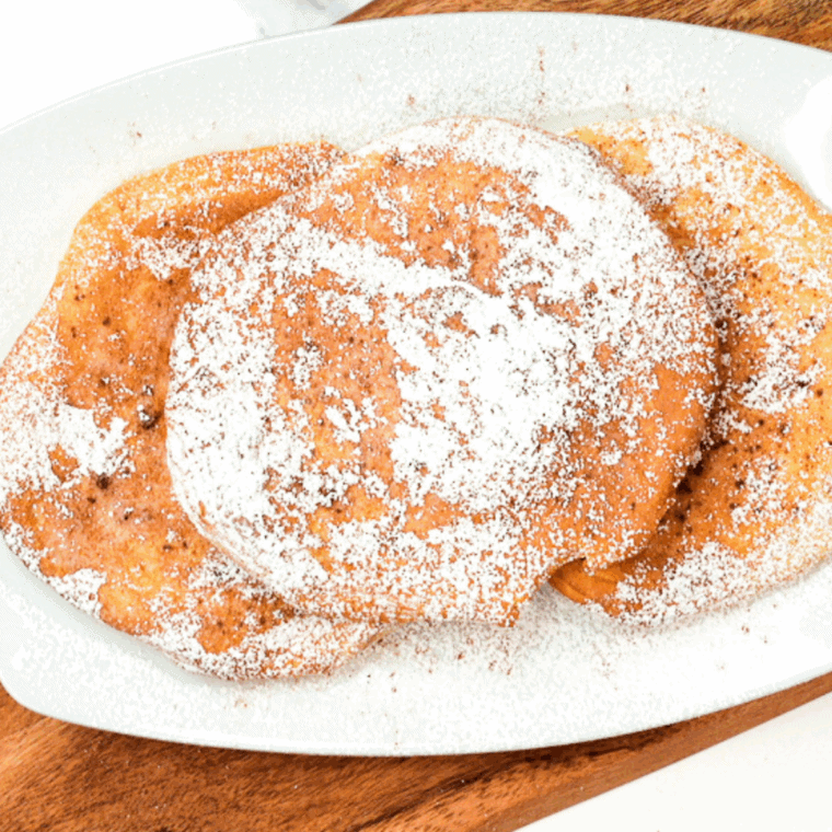Air fryer fried dough being drizzled with chocolate sauce and cinnamon sugar.