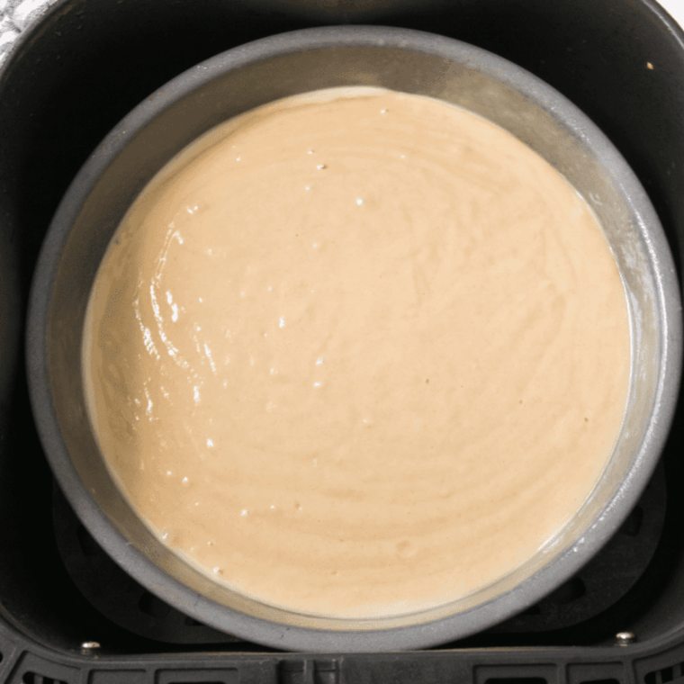 Air fryer cake cooking in basket and checking doneness with toothpick