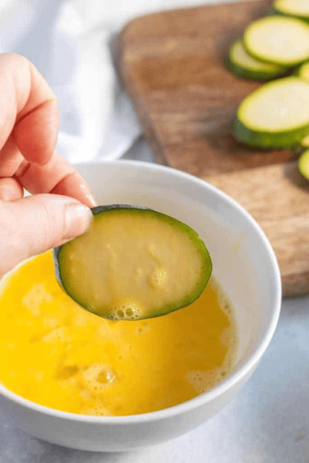 Zucchini slices being dipped into egg wash and coated with almond flour and Parmesan mixture for air fryer keto chips.