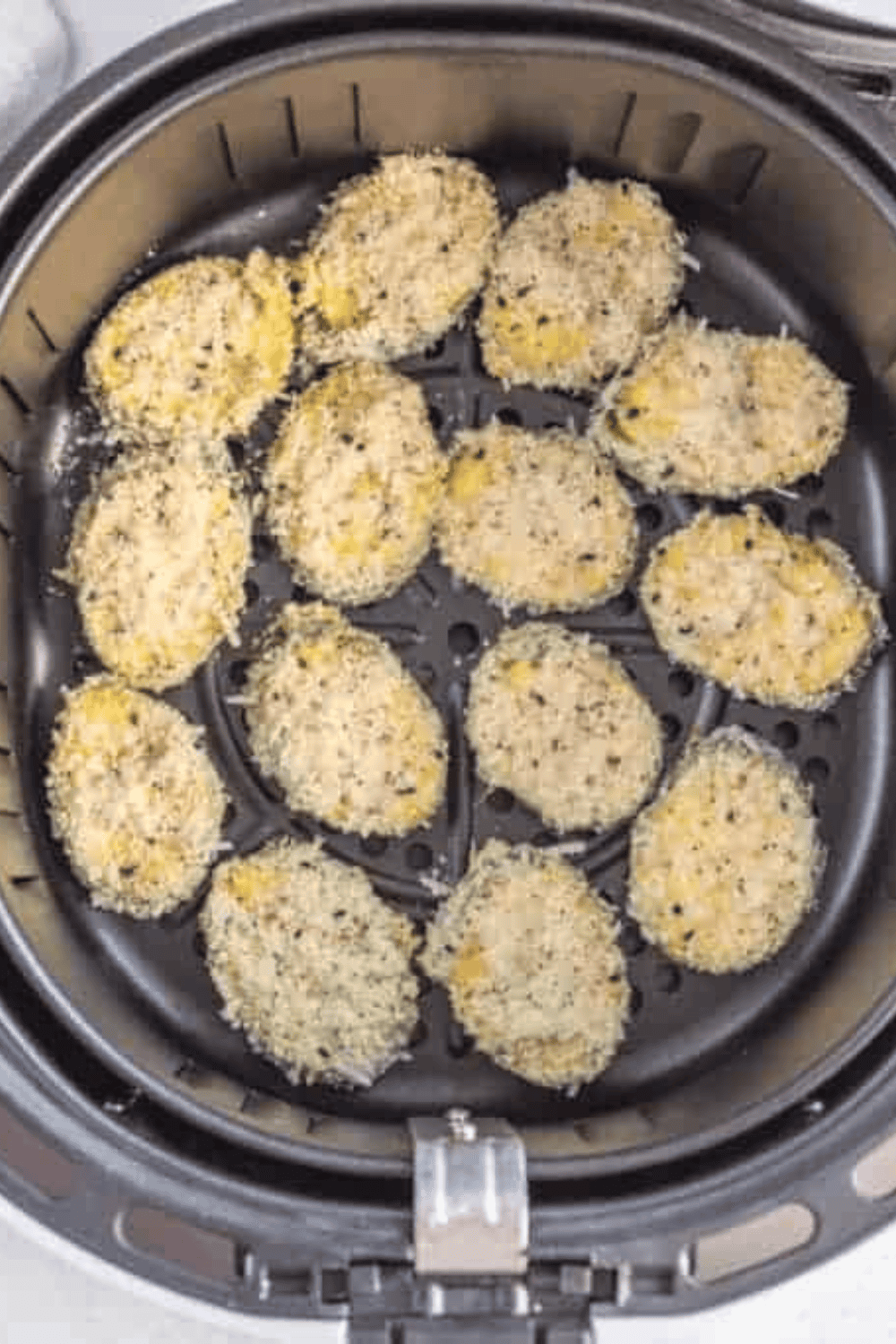 Zucchini chips arranged in an air fryer basket, being cooked to golden, crispy perfection.
