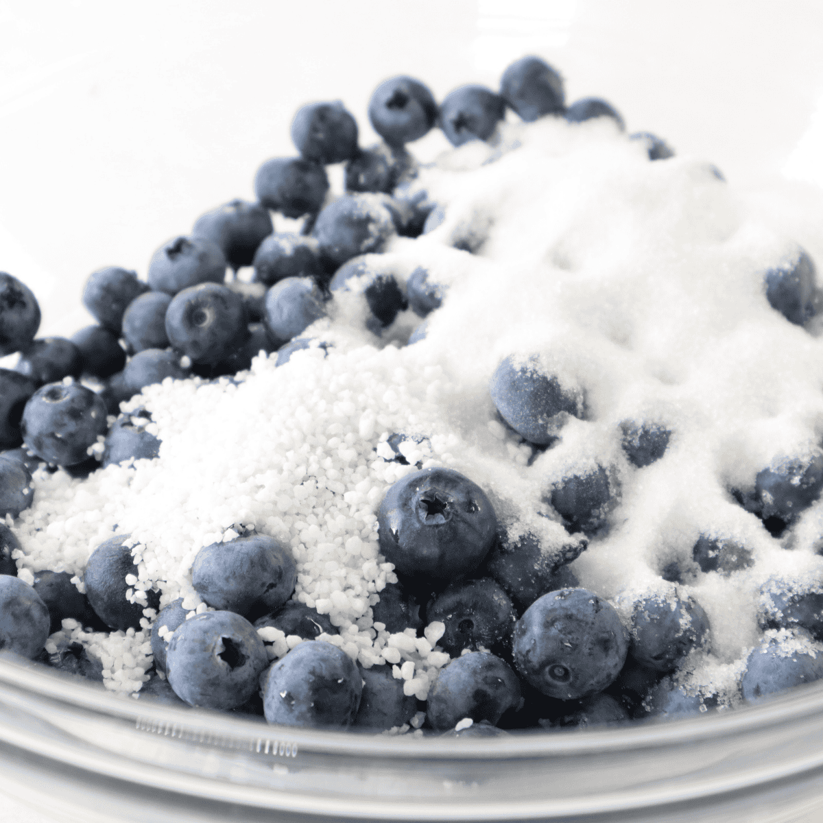 Fresh blueberries tossed with sugar, flour, and cinnamon in a mixing bowl