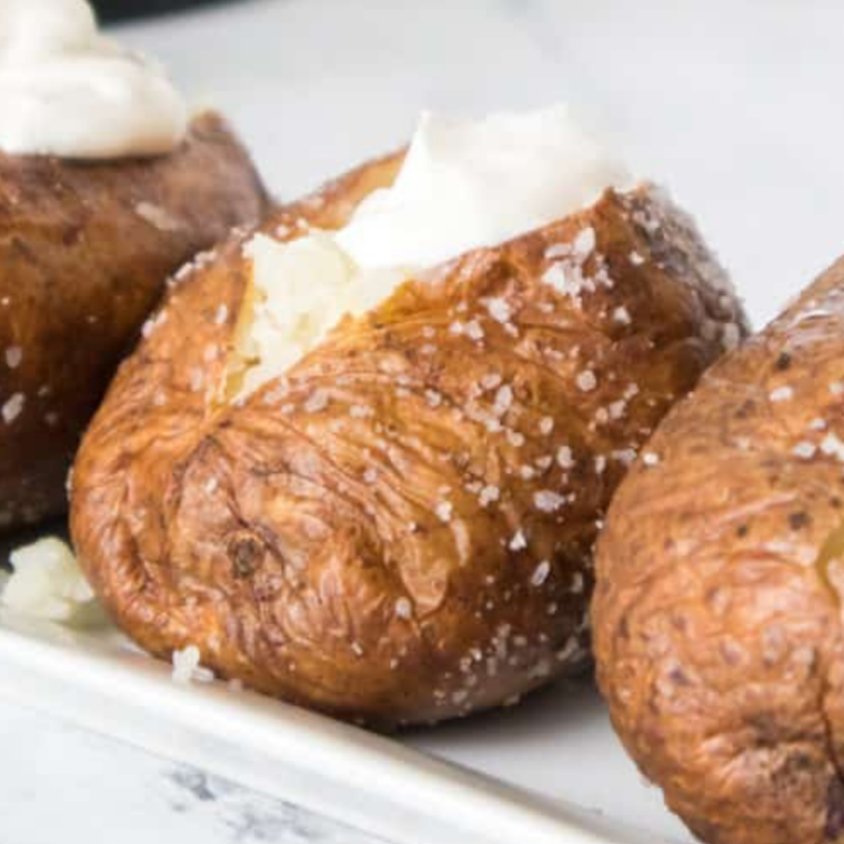 Plate of air fryer jacket potatoes with sour cream, bacon, and chopped chives