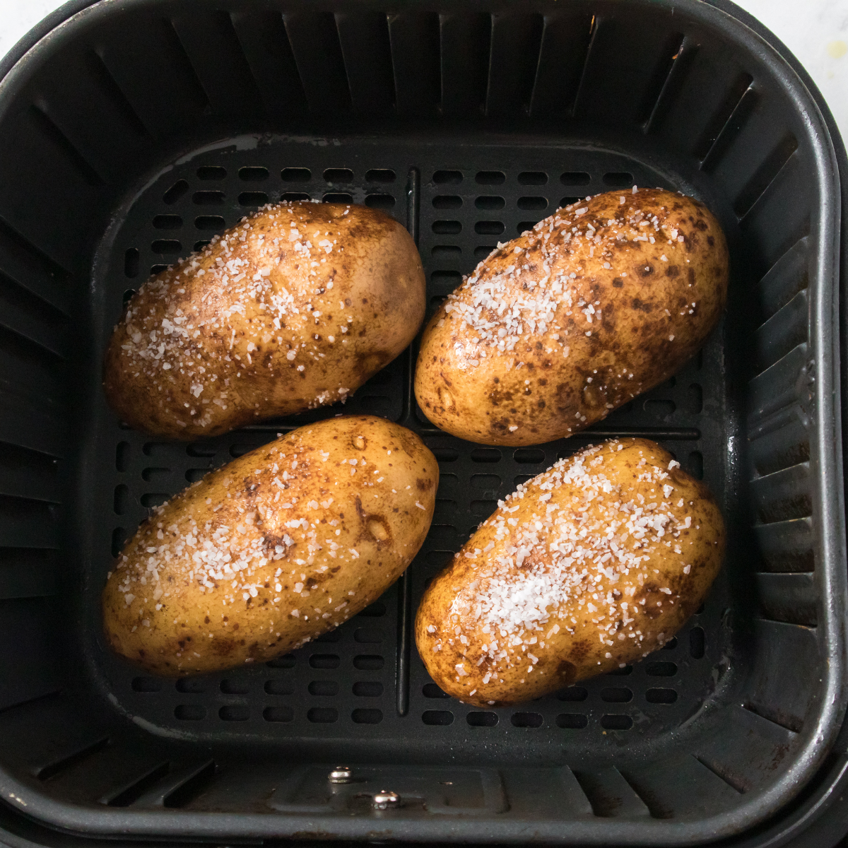 Four jacket potatoes spaced in a single layer in the air fryer basket