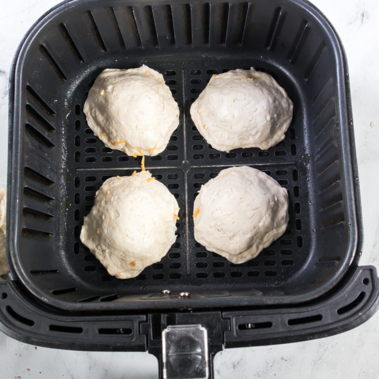 Filled air fryer sausage biscuits arranged in a single layer in the air fryer basket