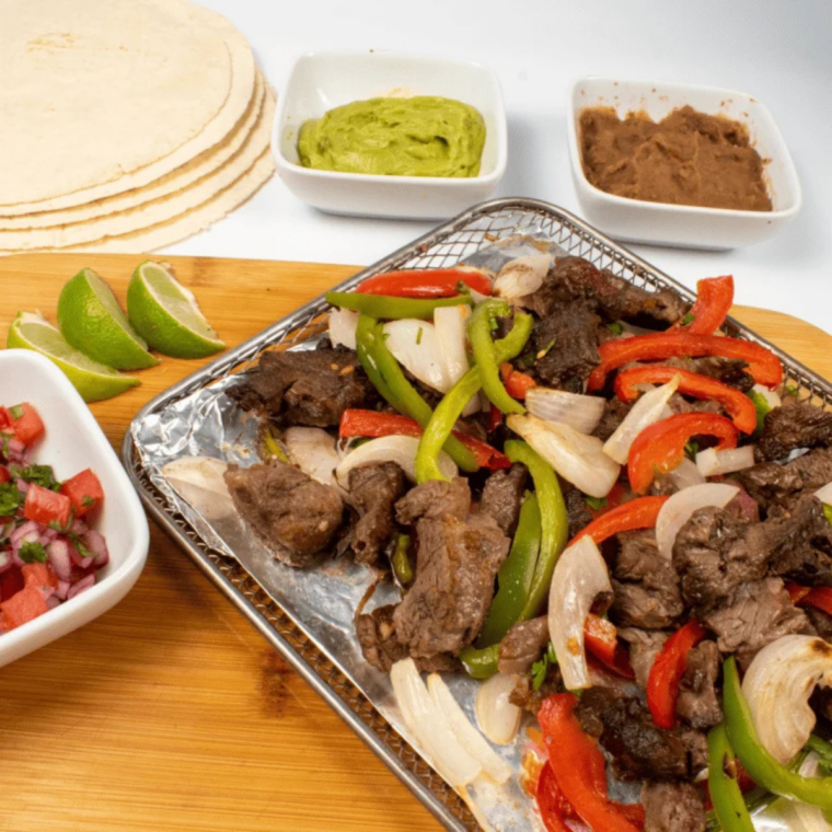 Two air fryer steak tacos on a plate with juicy ribeye slices, fresh toppings, and lime wedges