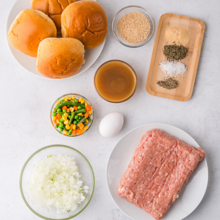Ground chicken breast, breadcrumbs, mayonnaise, lemon juice, garlic, and fresh herbs in bowls before mixing