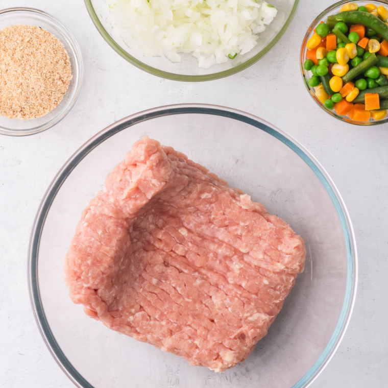 Ground chicken, breadcrumbs, mayonnaise, and fresh herbs combined in a large glass mixing bowl