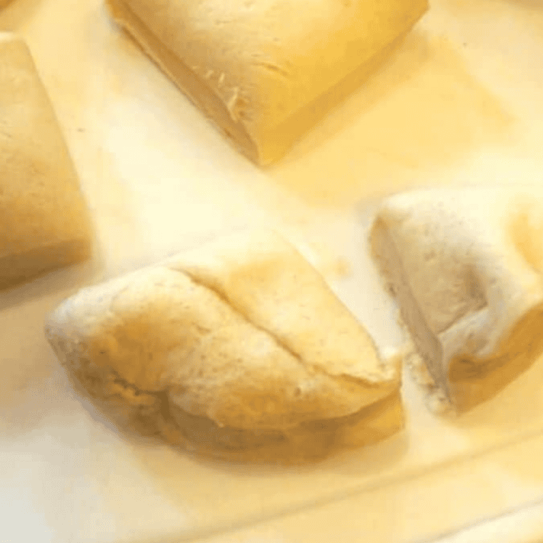 Refrigerated biscuit dough cut into quarters on a cutting board before coating in cinnamon sugar