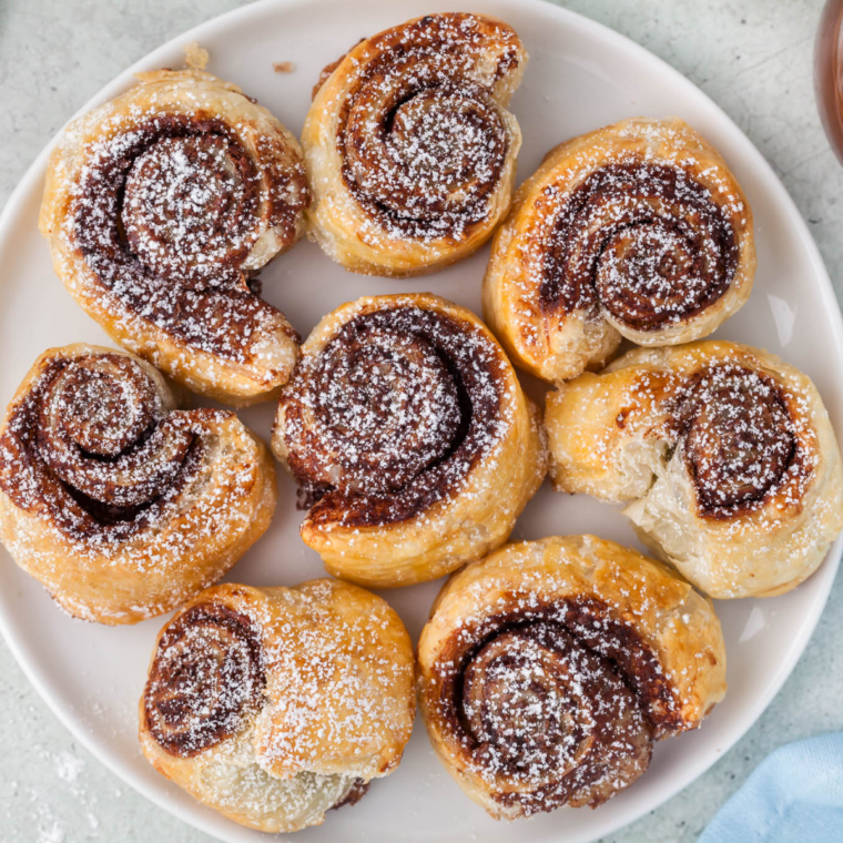 Golden air fryer Nutella puff pastry bites stacked on a white plate and dusted with powdered sugar