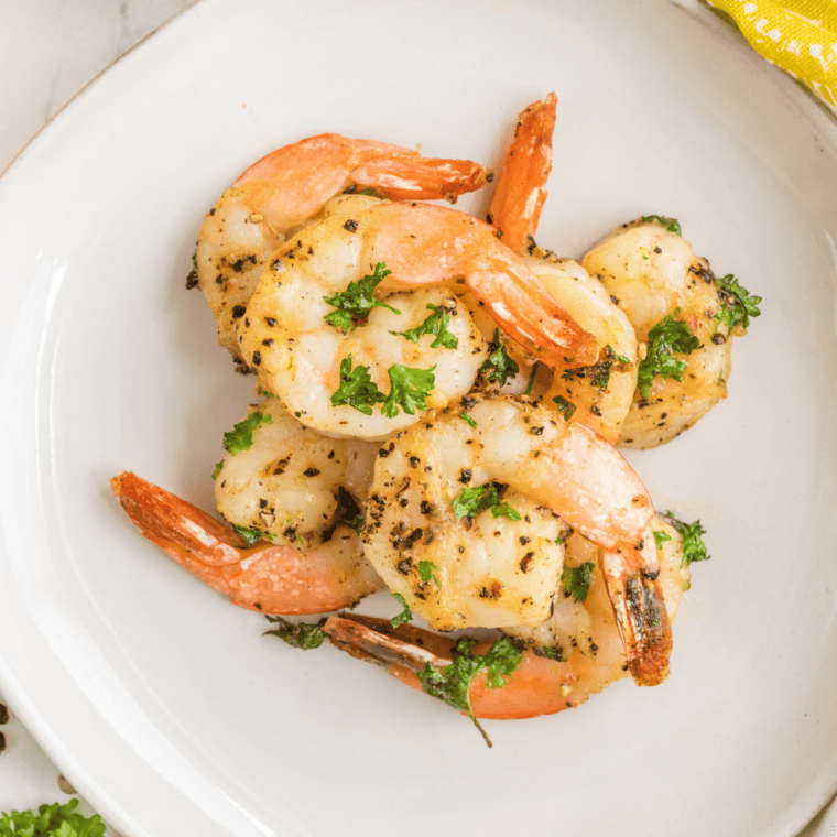Golden, garlicky colossal shrimp cooked in an air fryer, served on a plate with fresh herbs.