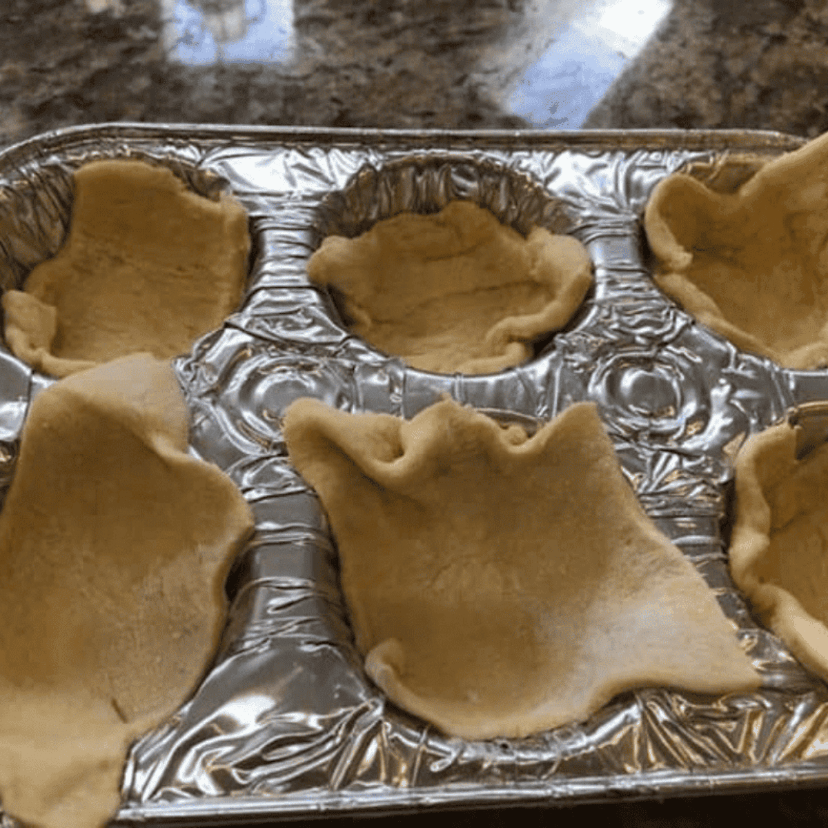 Greasing muffin tin and cutting crescent dough slightly larger to fit and fold over each cup