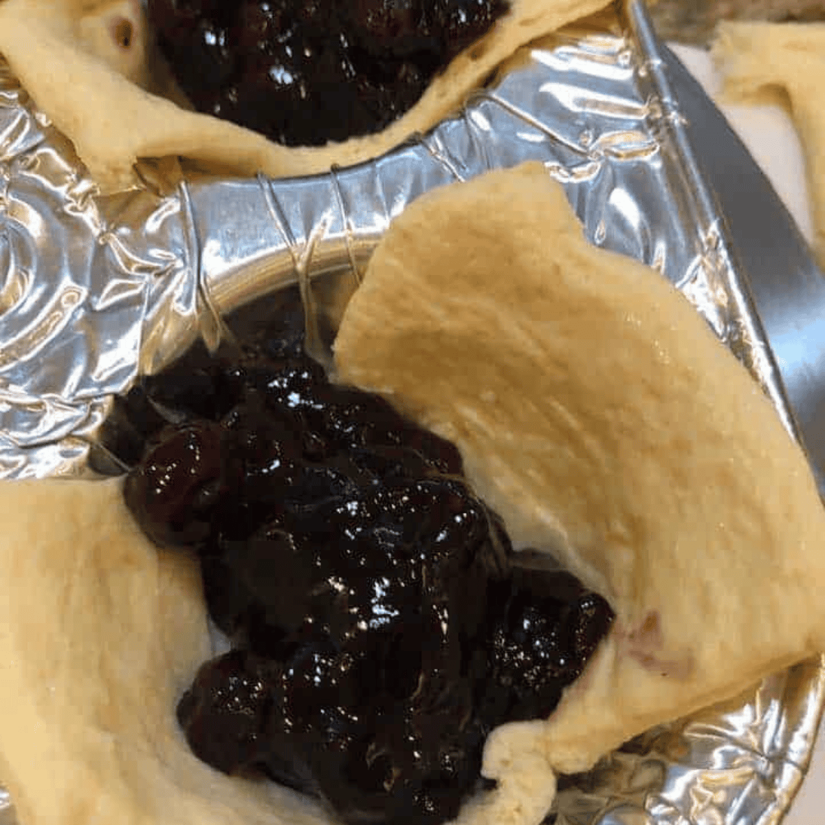 Scooping blueberry pie filling into crescent dough and folding edges to form a pocket