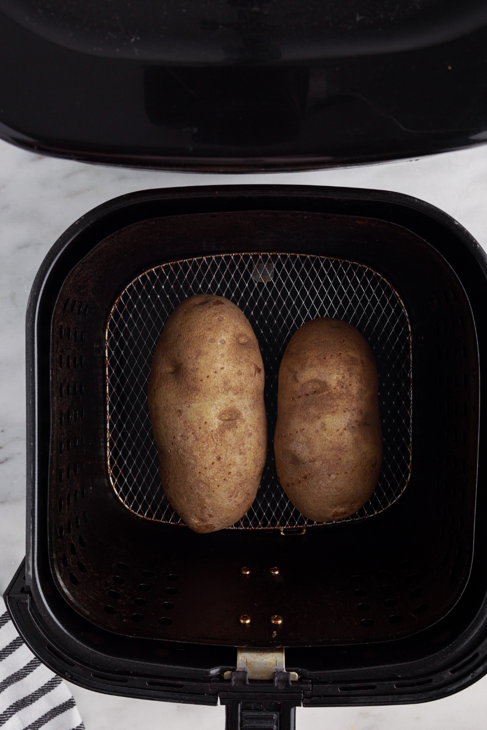 Air fryer baked potatoes cooking at 400°F with flipping halfway through until fork tender and fully cooked inside.