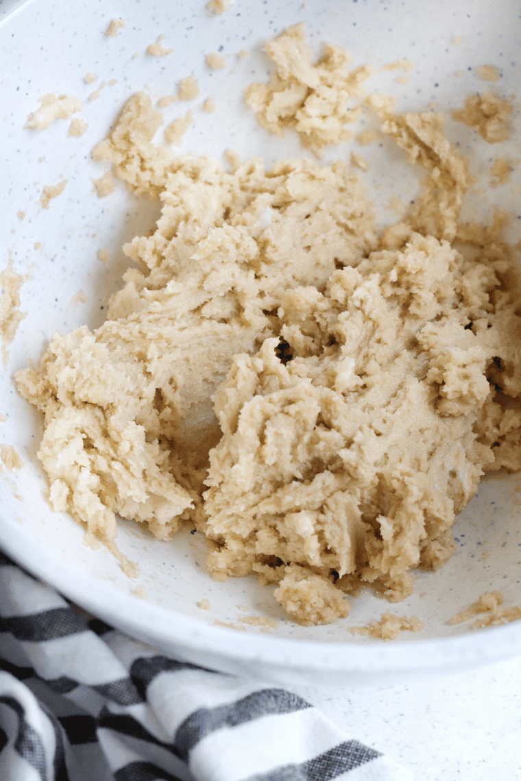 Mixing snickerdoodle dough with eggs and dry ingredients, then rolling cookies in cinnamon sugar.