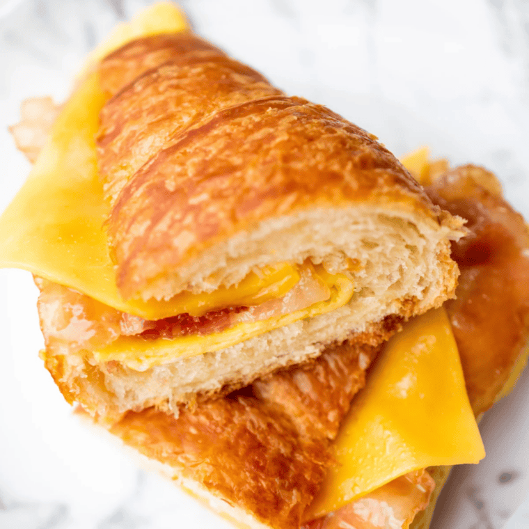 Air fryer bacon egg and cheese croissant cut in half showing candied bacon, a fried egg, and melted cheese