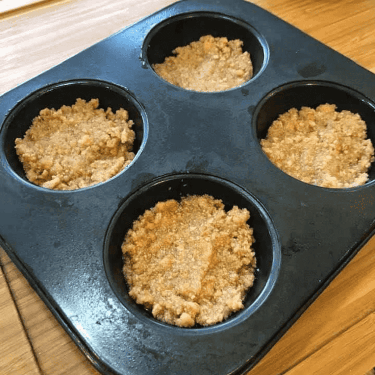 Graham cracker crust mixture pressed into the bottom of muffin liners in a cupcake tin