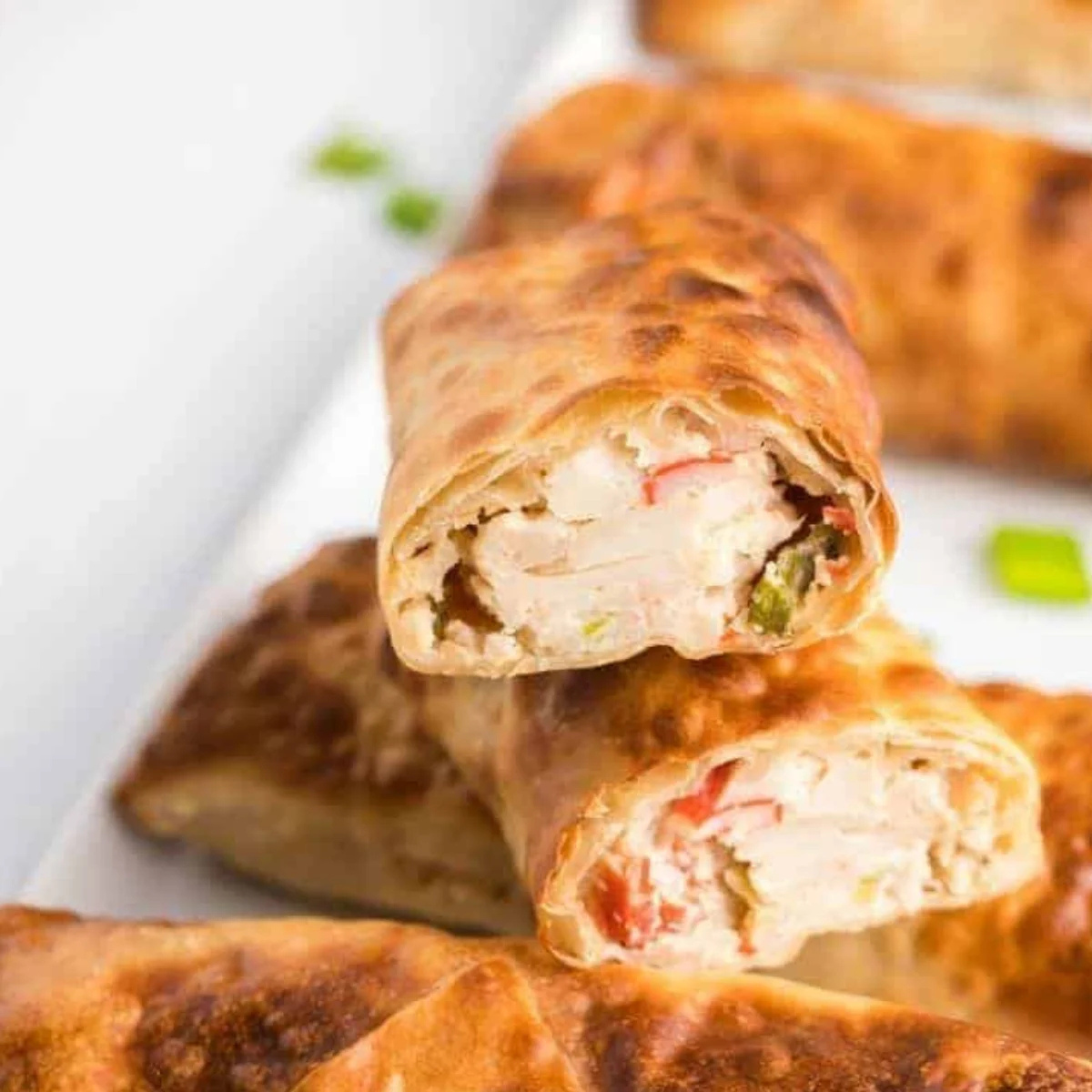 Plate of golden brown air fryer crab rangoon egg rolls with sweet chili dipping sauce