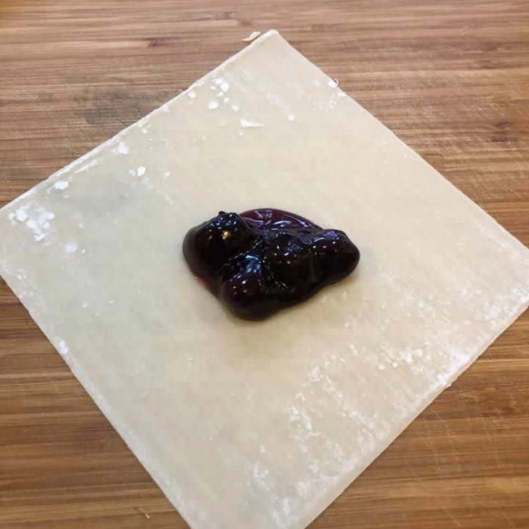 Spooning blueberry pie filling into the center of an egg roll wrapper