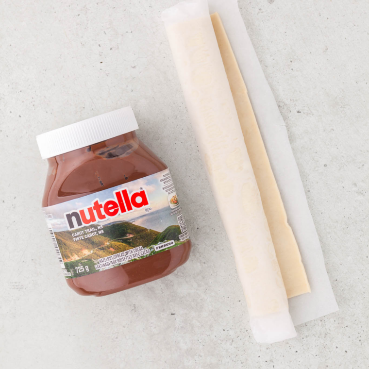 Wonton wrappers, a jar of Nutella, and powdered sugar arranged on a marble countertop