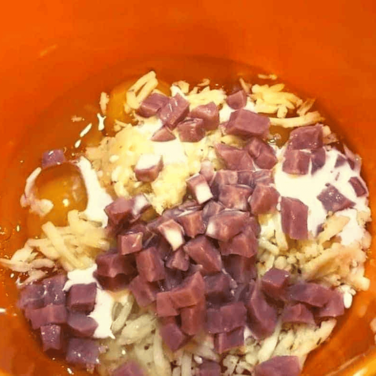 Whisking eggs, diced ham, shredded cheese, heavy cream, salt, and pepper together in a small mixing bowl for air fryer ham and cheese muffins.