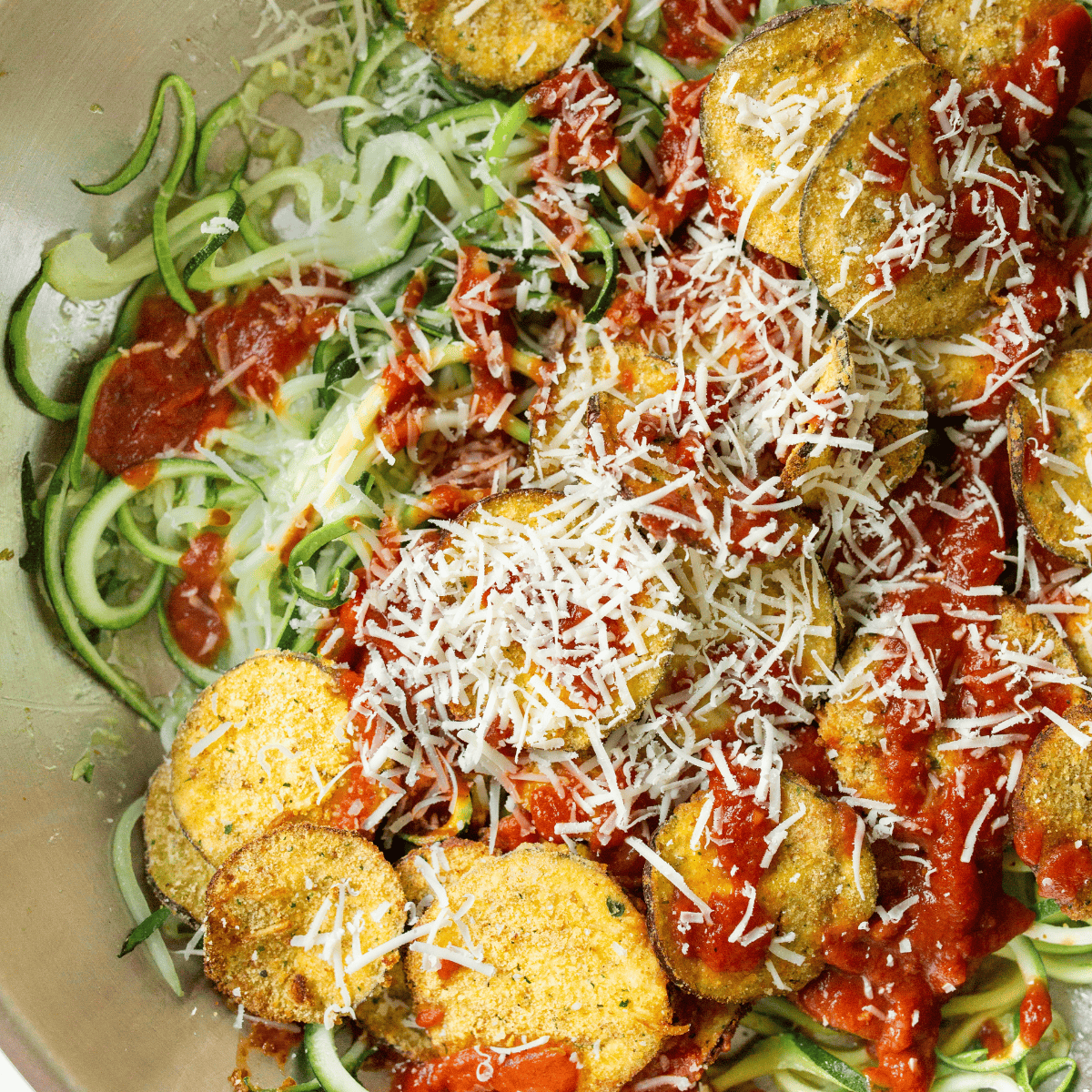 Plate of cooked zucchini noodles with homemade eggplant parmesan.