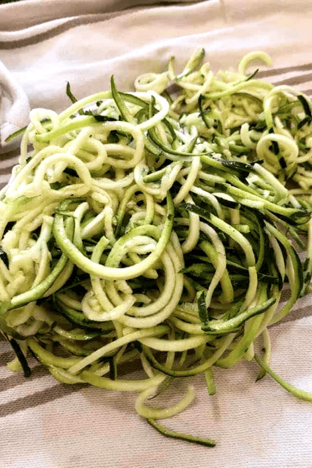Zucchini being spiralized into noodles and patted dry on a towel to remove excess moisture.