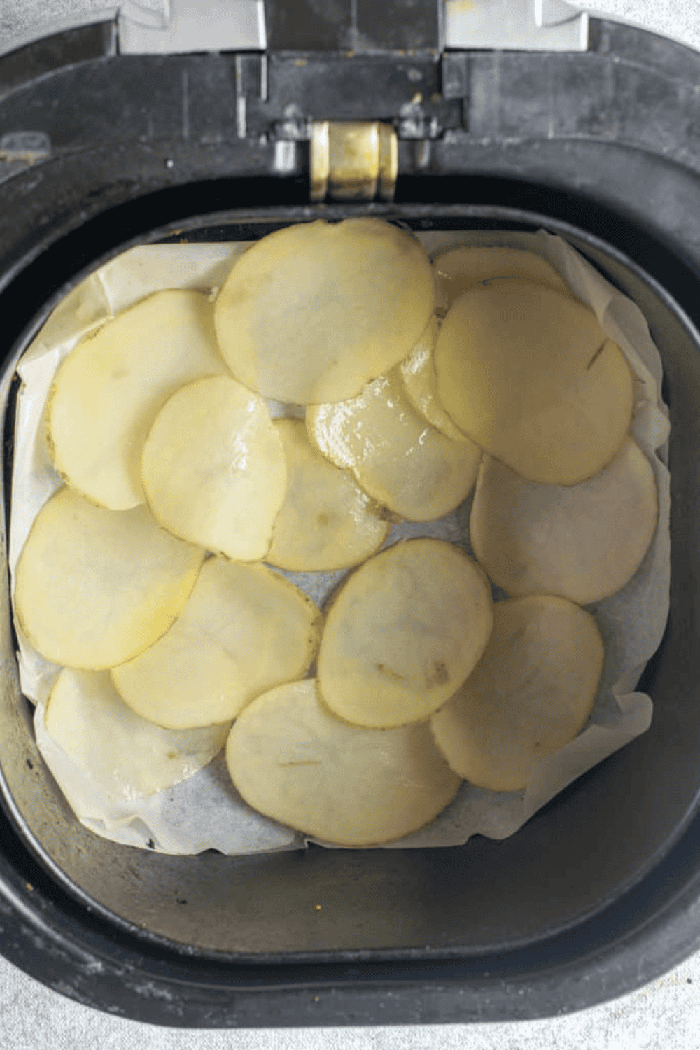 Seasoned potato slices in air fryer basket, ready for cooking.