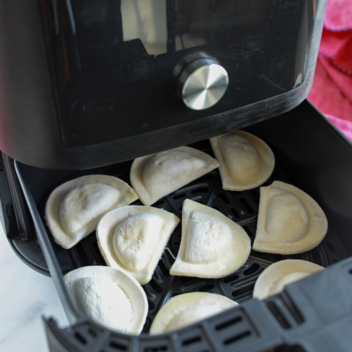 Frozen pierogies lightly coated with cooking oil, arranged in a single layer in the air fryer basket, cooking to golden and crispy perfection.