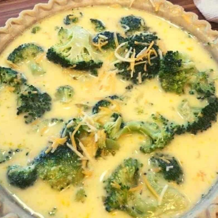 Broccoli and cheddar egg filling being poured into a par-baked pie crust in a tart pan