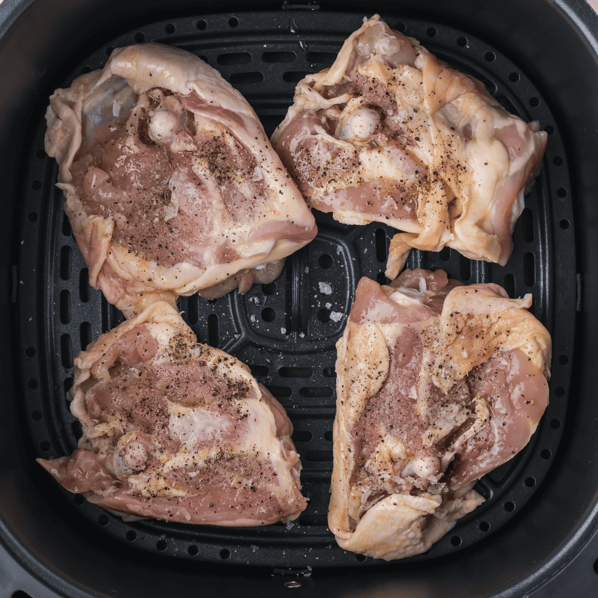 Seasoned Caribbean chicken thighs arranged skin side up in a single layer in the air fryer basket