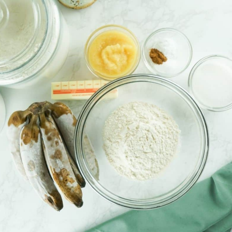 Ingredients for gluten-free banana bread including ripe bananas, gluten-free flour, applesauce, and vegan butter