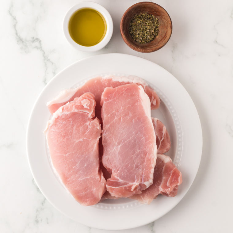 Pork chops, honey, minced garlic, lemon juice, olive oil, and sweet chili sauce laid out on a kitchen table