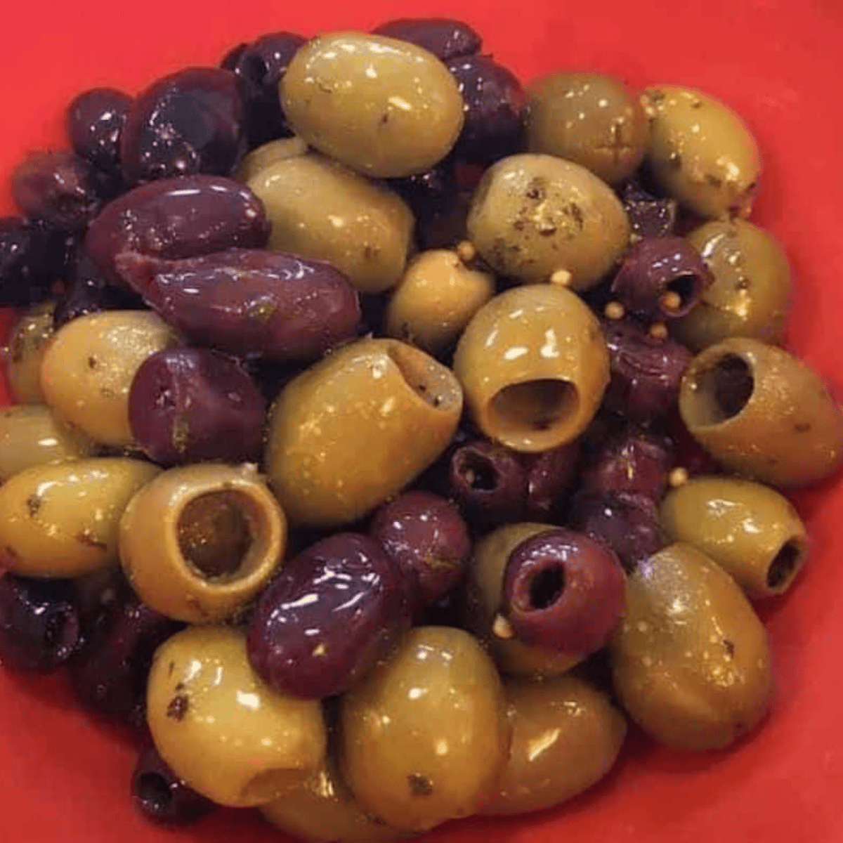 Mixed olives tossed in olive oil, garlic, oregano, fennel seeds, red pepper, salt, and black pepper in a large bowl.