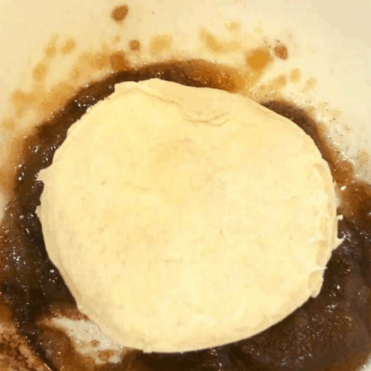 Small bowl with butter, brown sugar, and cinnamon mixture, dipping biscuit into it and placing in baking pan