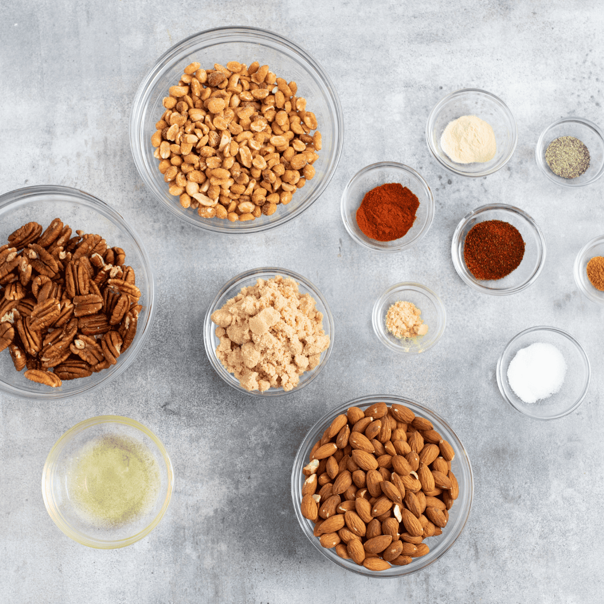 Raw mixed nuts, olive oil, dried rosemary, oregano, thyme, kosher salt, and black pepper in bowls