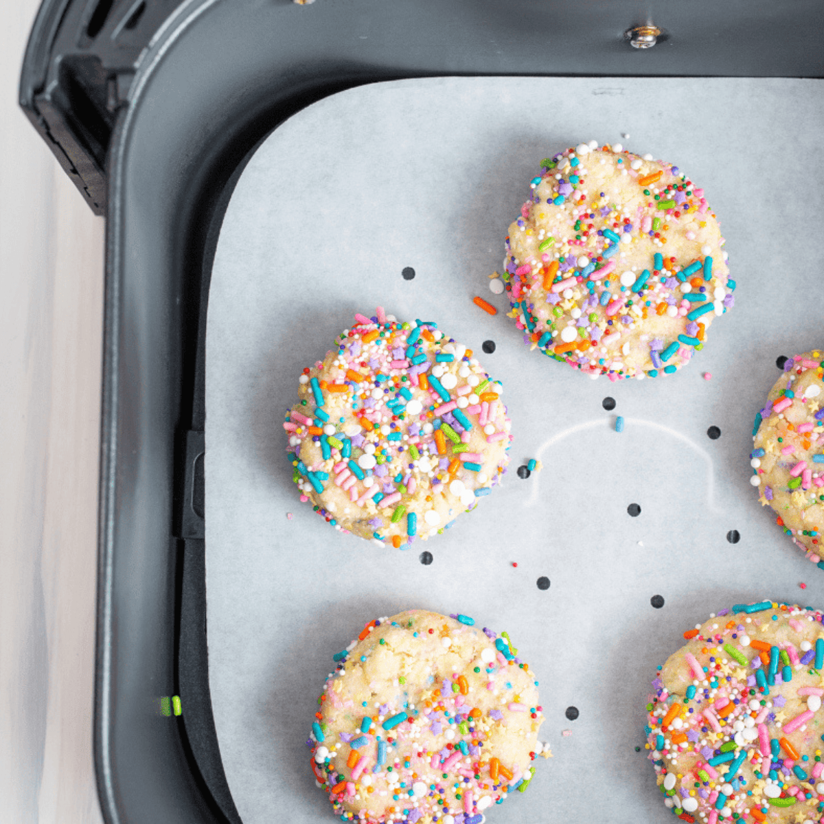 Pre-cut, perforated parchment paper liners being placed into an empty air fryer basket before food is added.