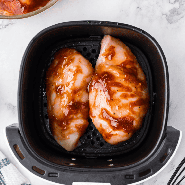 Seasoned chicken breasts in a single layer in the air fryer basket before cooking
