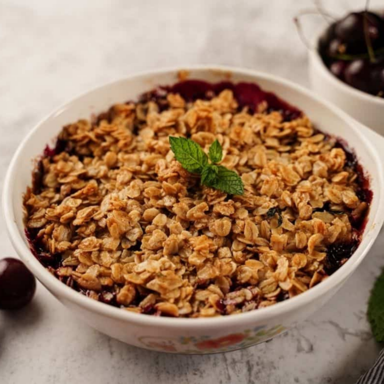 Finished cherry crumble served warm with a scoop of vanilla ice cream melting over the top.