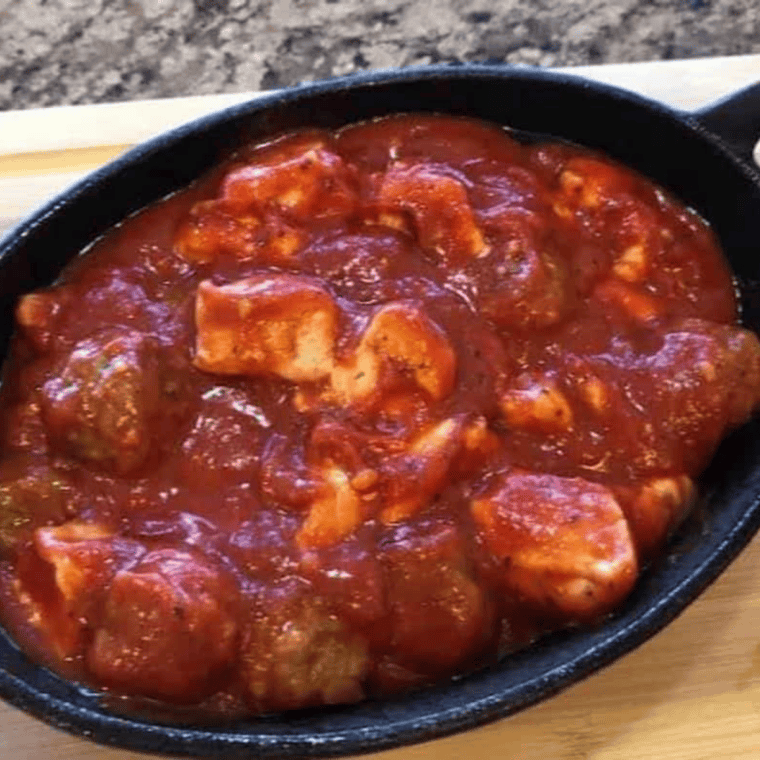 Meatballs and biscuit dough pieces tossed with marinara sauce in a large mixing bowl