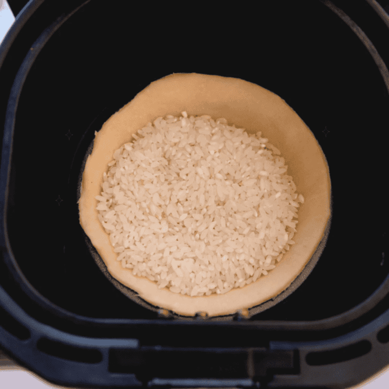 Unbaked pie crust lined with foil and pie weights in the air fryer basket